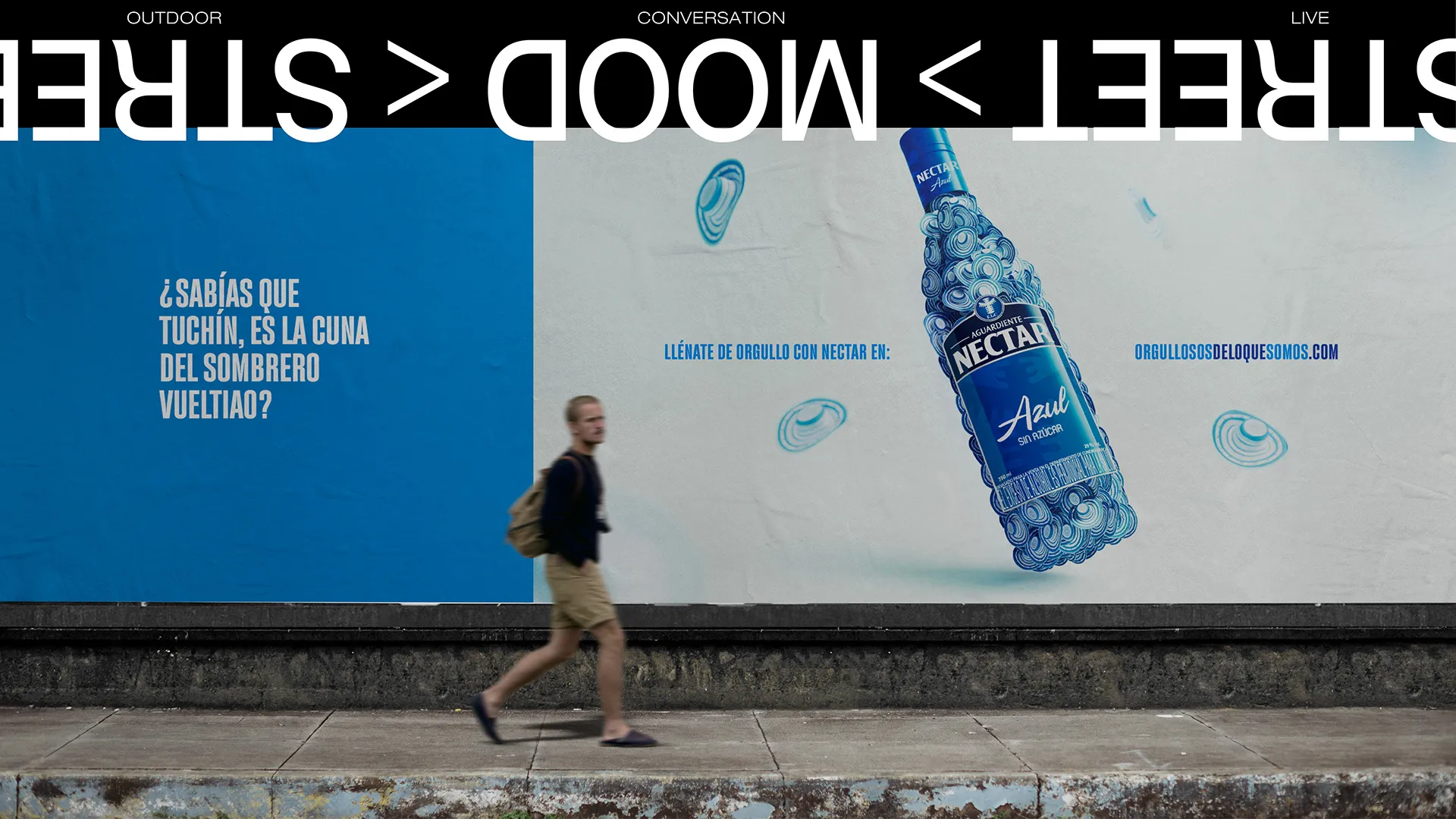 Valla en la calle con la botella azul de Néctar y una persona caminando