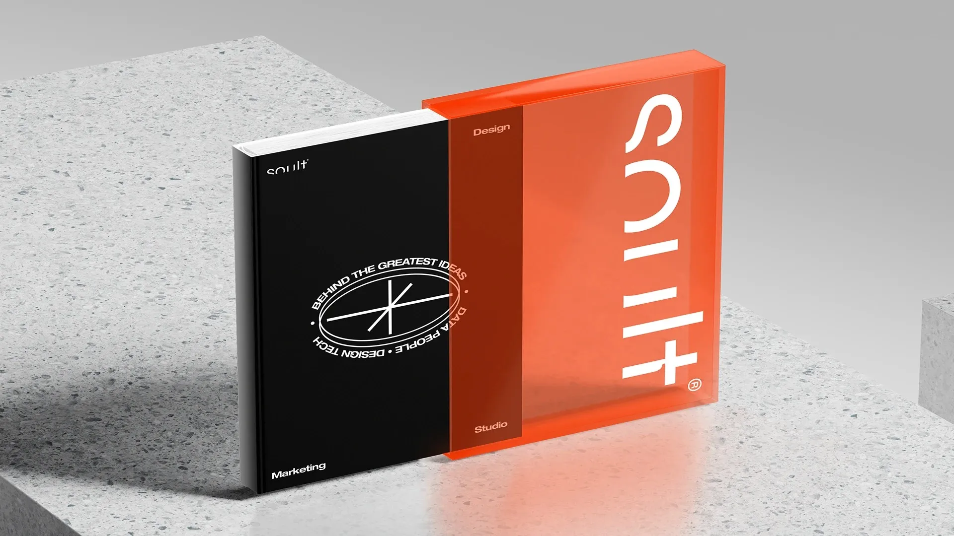 Libro negro de Soult con el sello Behind the greatest ideas junto a un estuche naranja translúcido con el logo, sobre una superficie de piedra