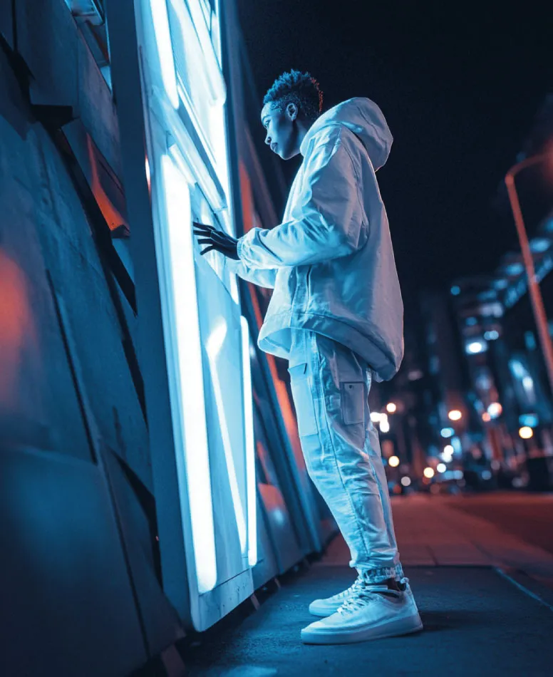 Joven con chaqueta blanca toca un panel de luz azul en una calle de noche